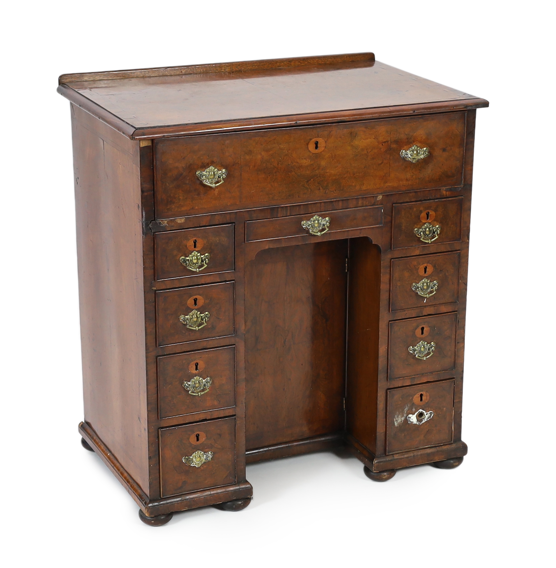 An early 18th century walnut kneehole secretaire desk, with quarter veneered top and fall front drawer opening to reveal pigeon holes and drawers, over eight further drawers surrounding a central recessed cupboard, on pa